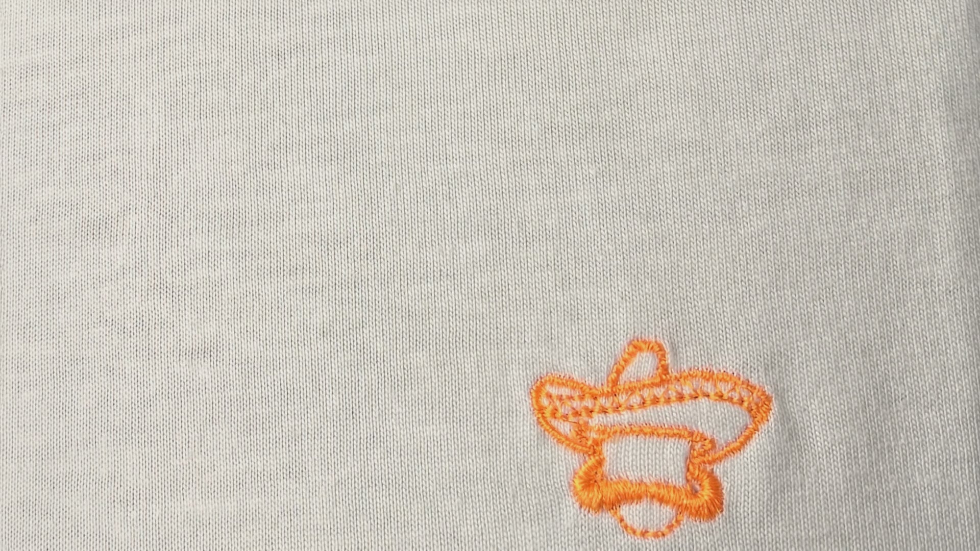 Vídeo macro del bordado en naranja flúor de la camiseta Class blanca de Knockout Couture, se aprecian los hilos y el algodón orgánico